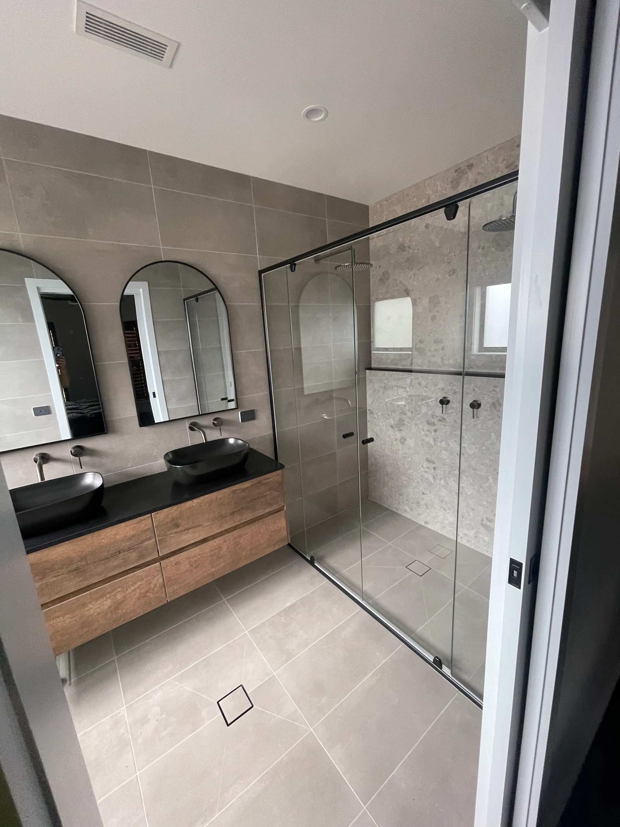 Modern bathroom with timber double vanity, black vessel sinks and glass walk-in shower