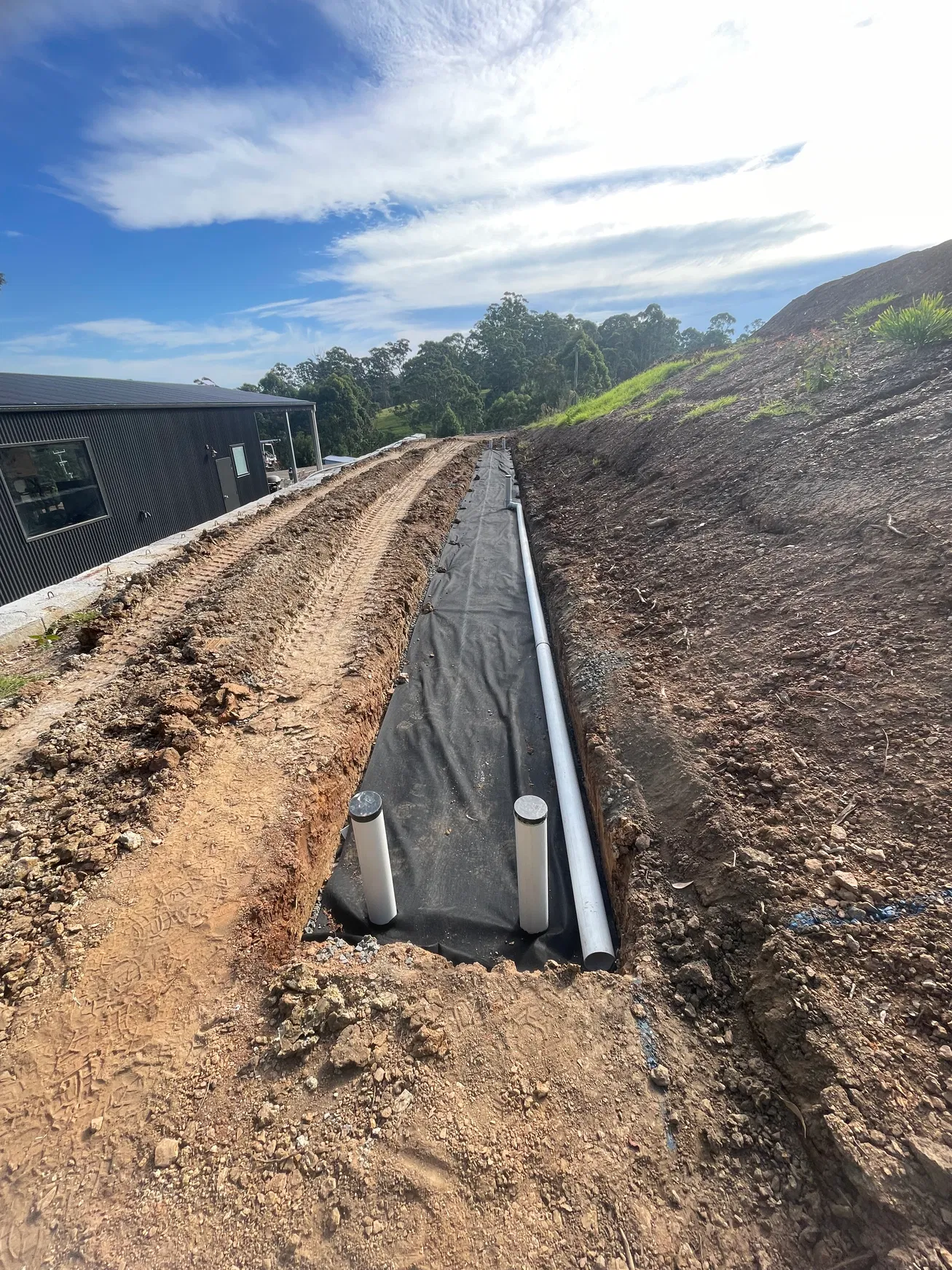 Fabric-lined drainage trench with white PVC pipe on hillside site