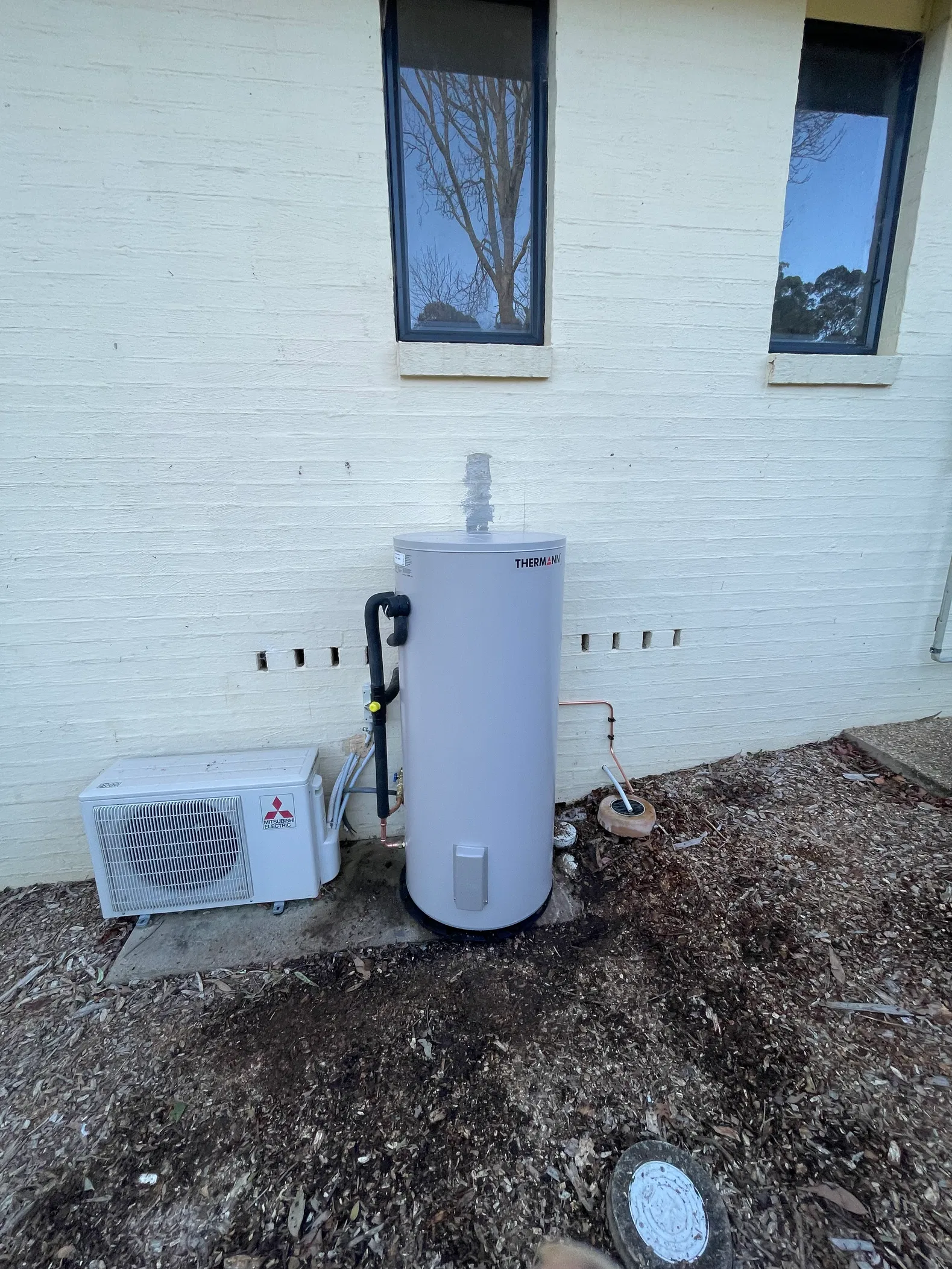 Mitsubishi heat pump and Thermann hot water tank installed against brick wall