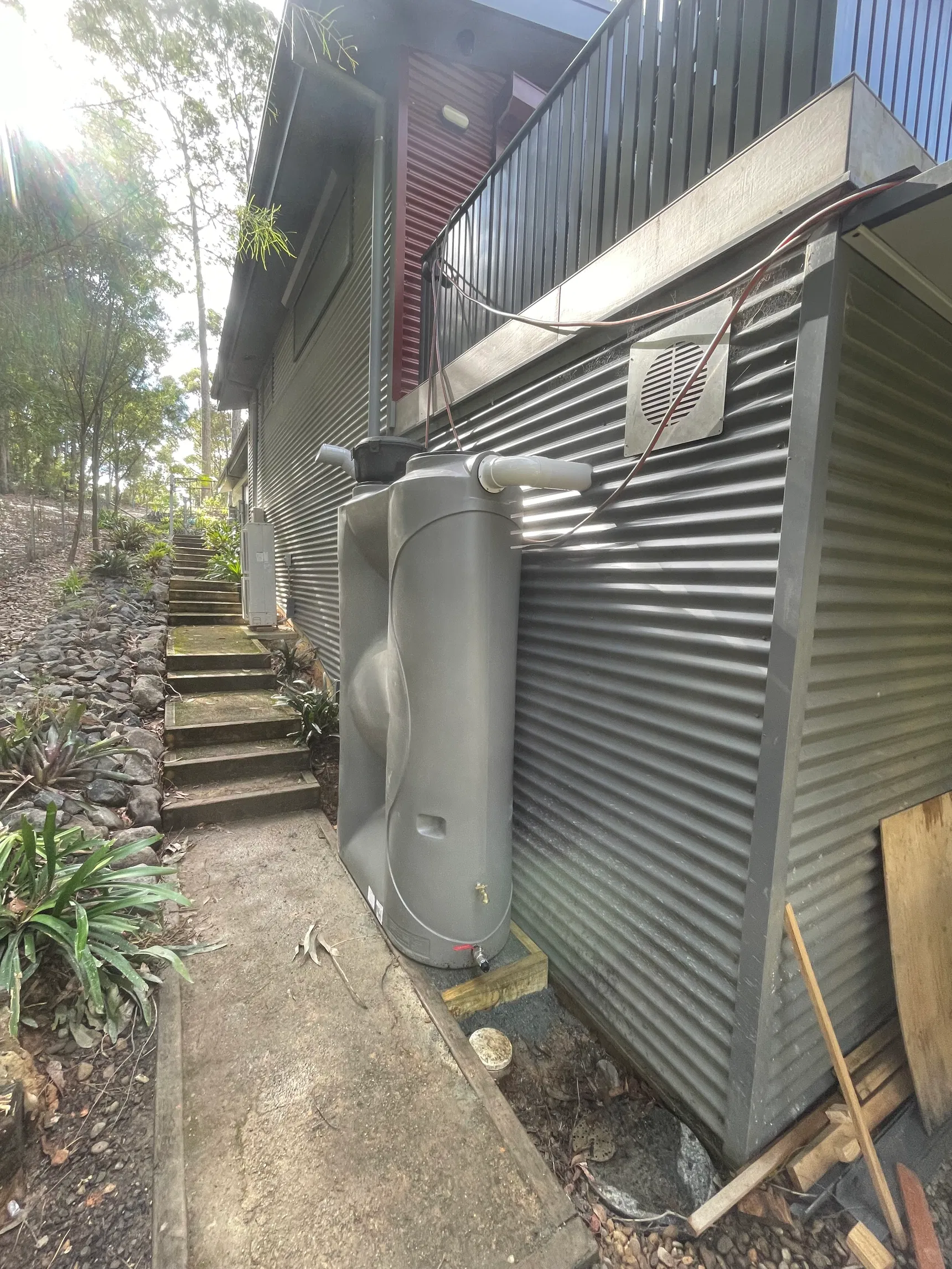 Slimline grey rainwater tank installed beside house cladding